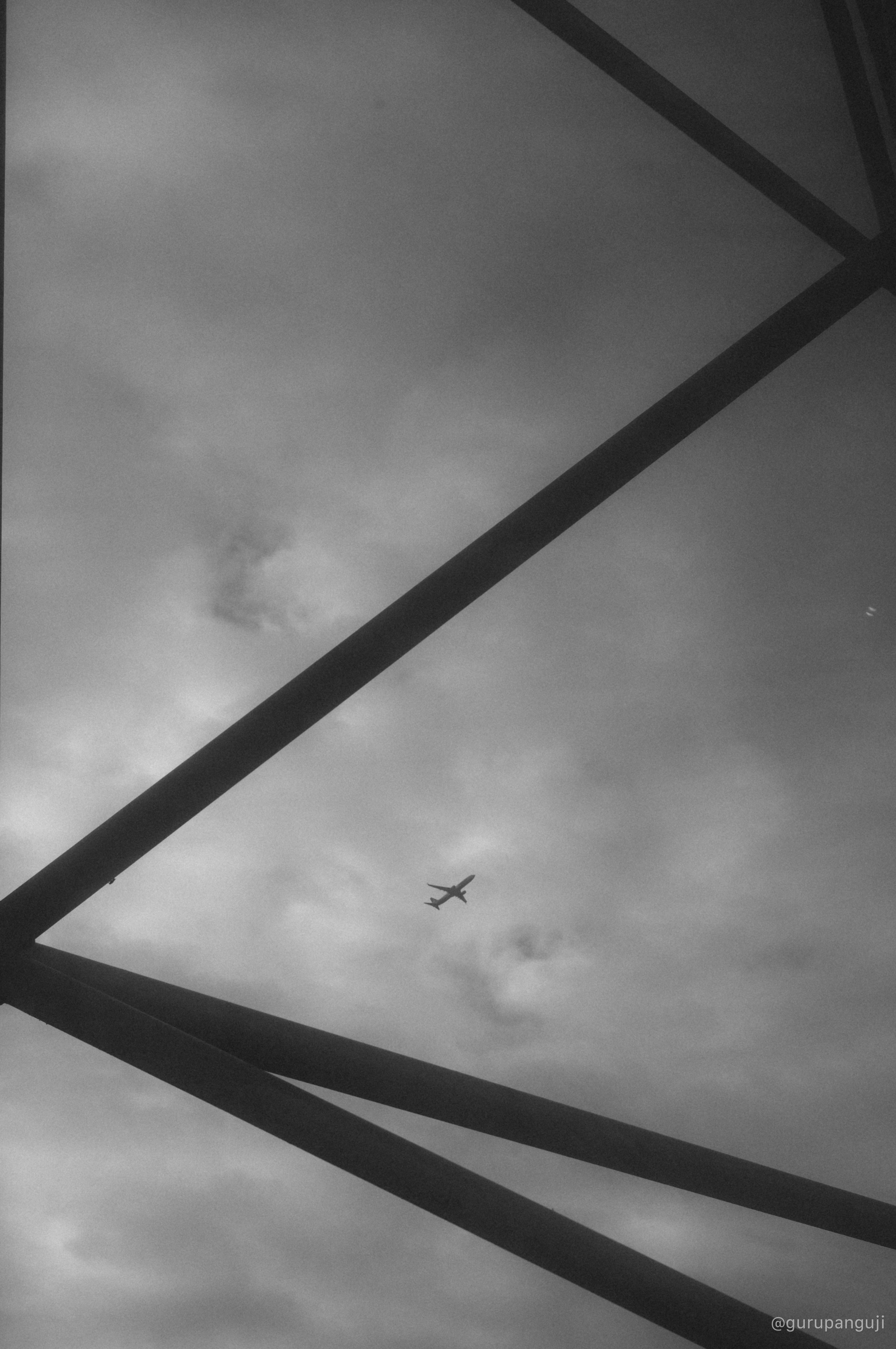 Airplane framed in diagonal steel structure against cloudy sky